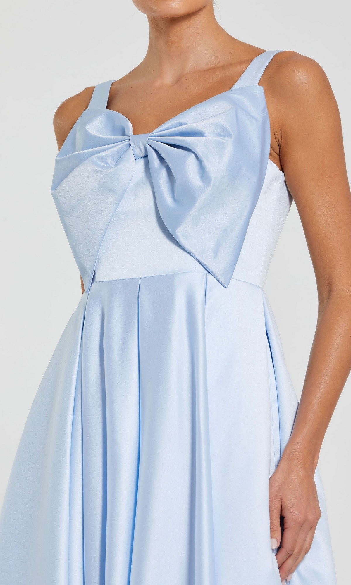 A woman in the Mac Duggal 2288 Midi Wedding Guest Dress—sleeveless, light blue satin with a statement bow on the chest and flared skirt—makes a chic choice for any wedding.