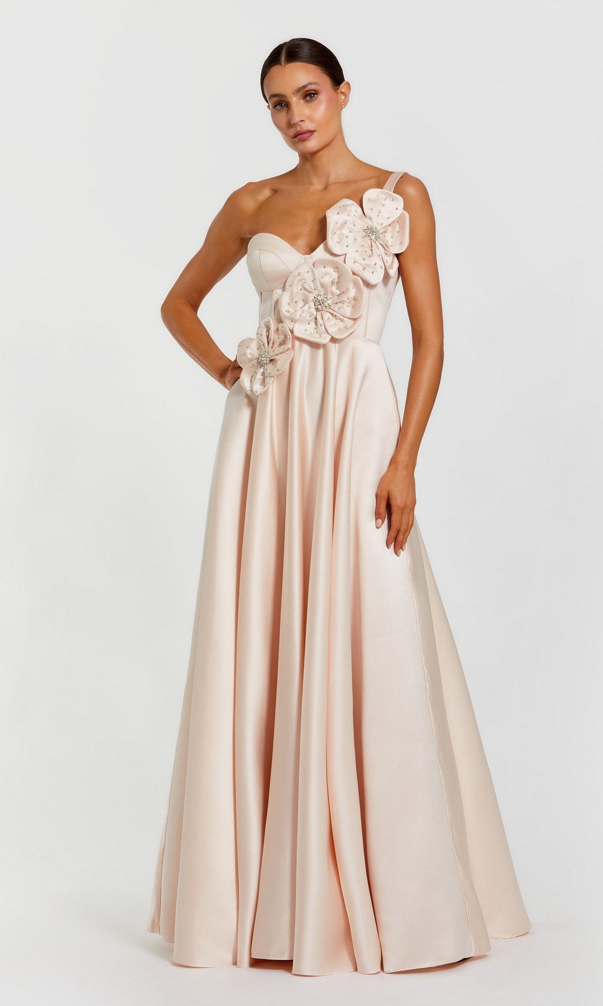 A woman wearing the Mac Duggal 2292 Long Formal Dress in oyster—a floor-length, satin, one-shoulder gown with large 3D floral appliques on the bodice—stands against a plain white background.