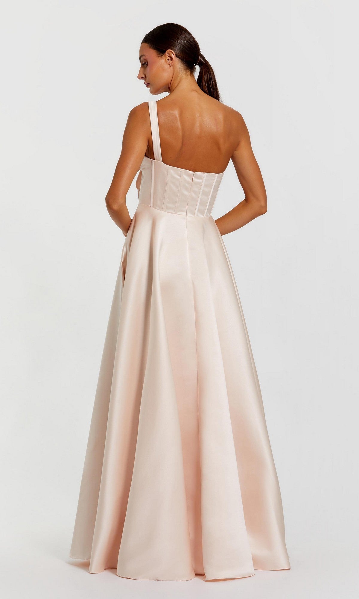 A woman is seen from behind, standing against a plain background, wearing the Mac Duggal 2292 long formal dress in light pink, featuring a floor-length design with a fitted, structured bodice and a single shoulder strap.