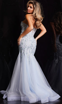 A woman poses in the Jovani Strapless Long Light Blue Prom Dress 22924, featuring floral embellishments and a tulle mermaid train, set against a dark background.
