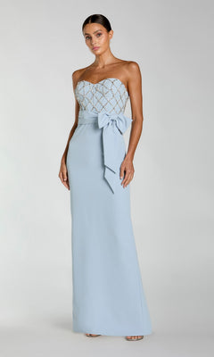 A woman models the Mac Duggal 2294 Strapless Sweetheart Formal Gown with a fitted lattice bodice and large waist bow, standing against a plain background.