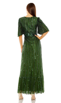 A woman stands with her back to the camera, wearing the Long Formal Dress 23010 by Mac Duggal—an emerald green, floor-length sequin gown with short sleeves and beige heels.