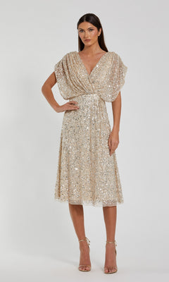 A woman stands against a plain white background wearing the Mac Duggal 23027 Knee Length Party Dress in Nude Silver, featuring short sleeves, sparkling sequins, a flattering v-neck bodice, and matching ankle-strap heels.