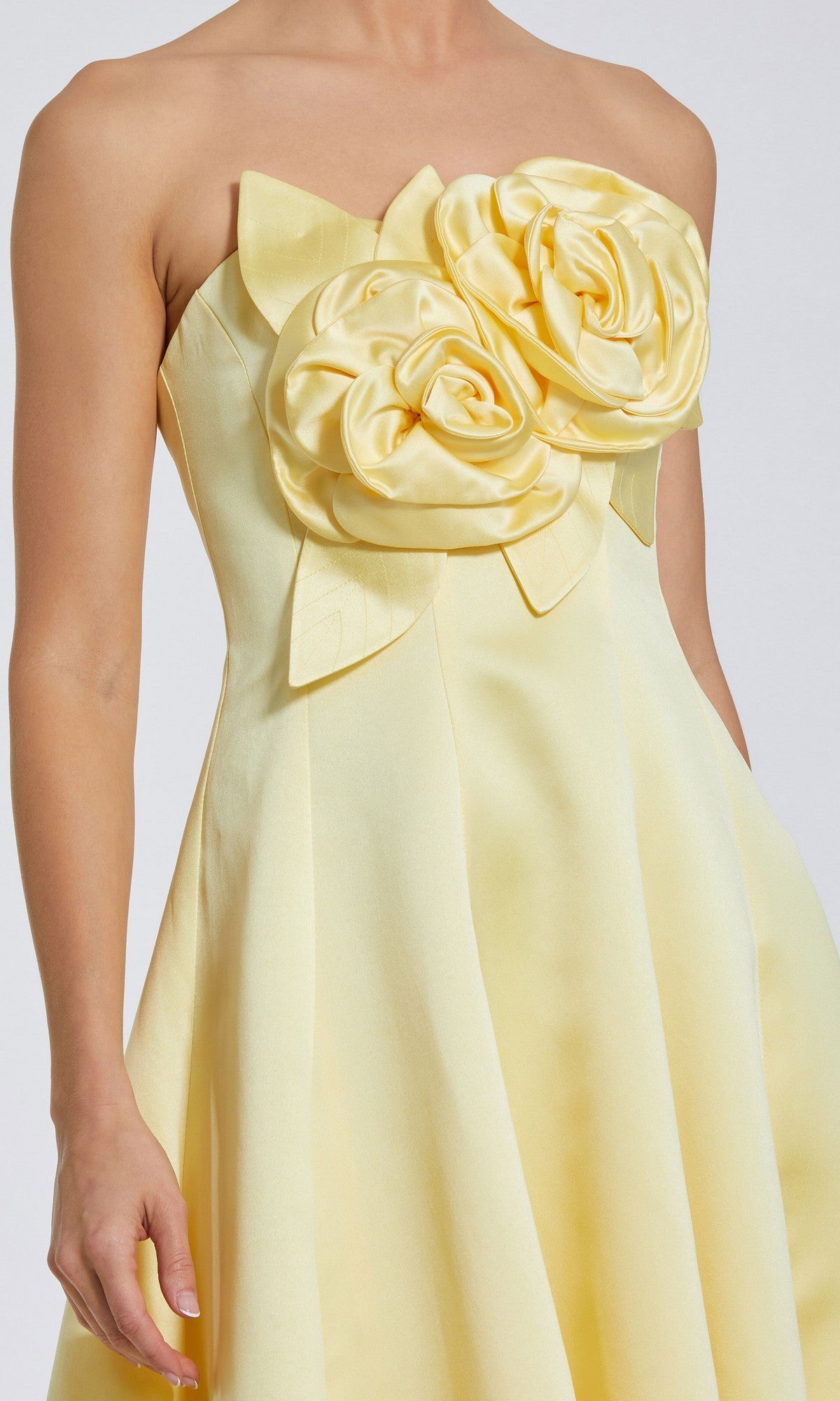 The Mac Duggal 2303 High-Low Formal Dress is a strapless yellow satin gown with two 3D floral accents on the bodice and a flared skirt.