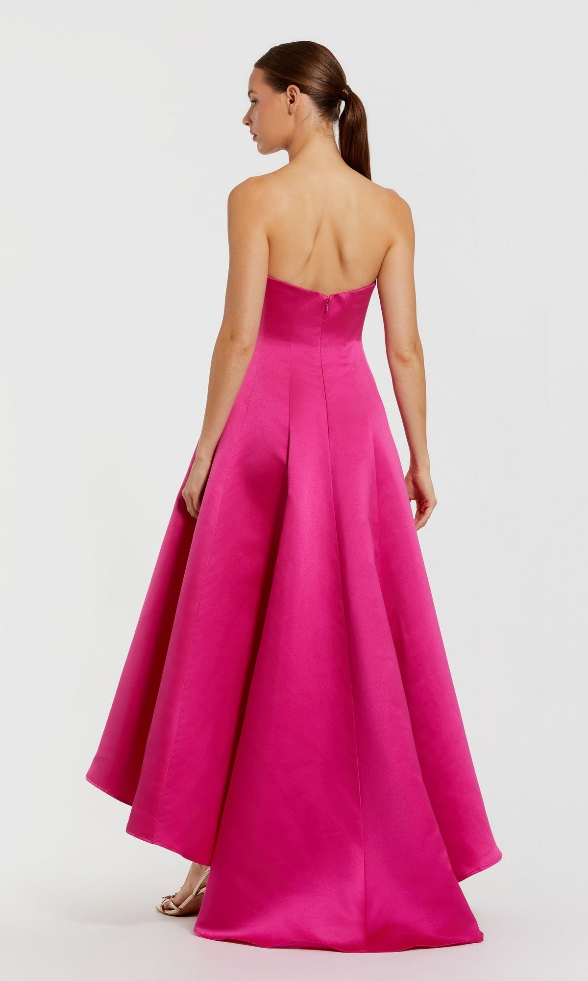 A woman faces away, wearing the Mac Duggal 2303 High-Low Formal Dress—a bright pink, strapless satin gown with a flared skirt—her hair styled in a low ponytail.