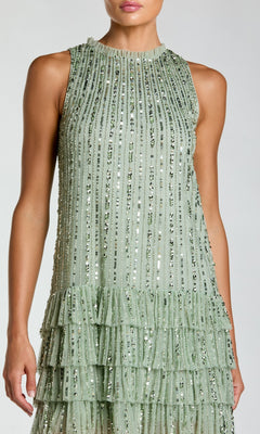 A woman wearing the Mac Duggal 23030 short party dress, featuring a sleeveless bodice, light green fabric with vertical sequin stripes, and a tiered ruffle skirt.