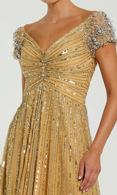 A woman wears the Mac Duggal 23042 Short Sleeve Gold Formal Dress—an elegant sequin evening gown with bead embellishments and ruched bodice, perfect for special occasions.