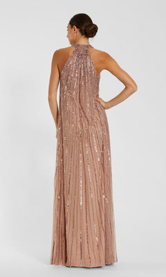 A woman stands with her back to the camera wearing the Mac Duggal 23043 long formal dress in blush, featuring vertical sequin embellishments, a high neckline, and floor-length embellished mesh.