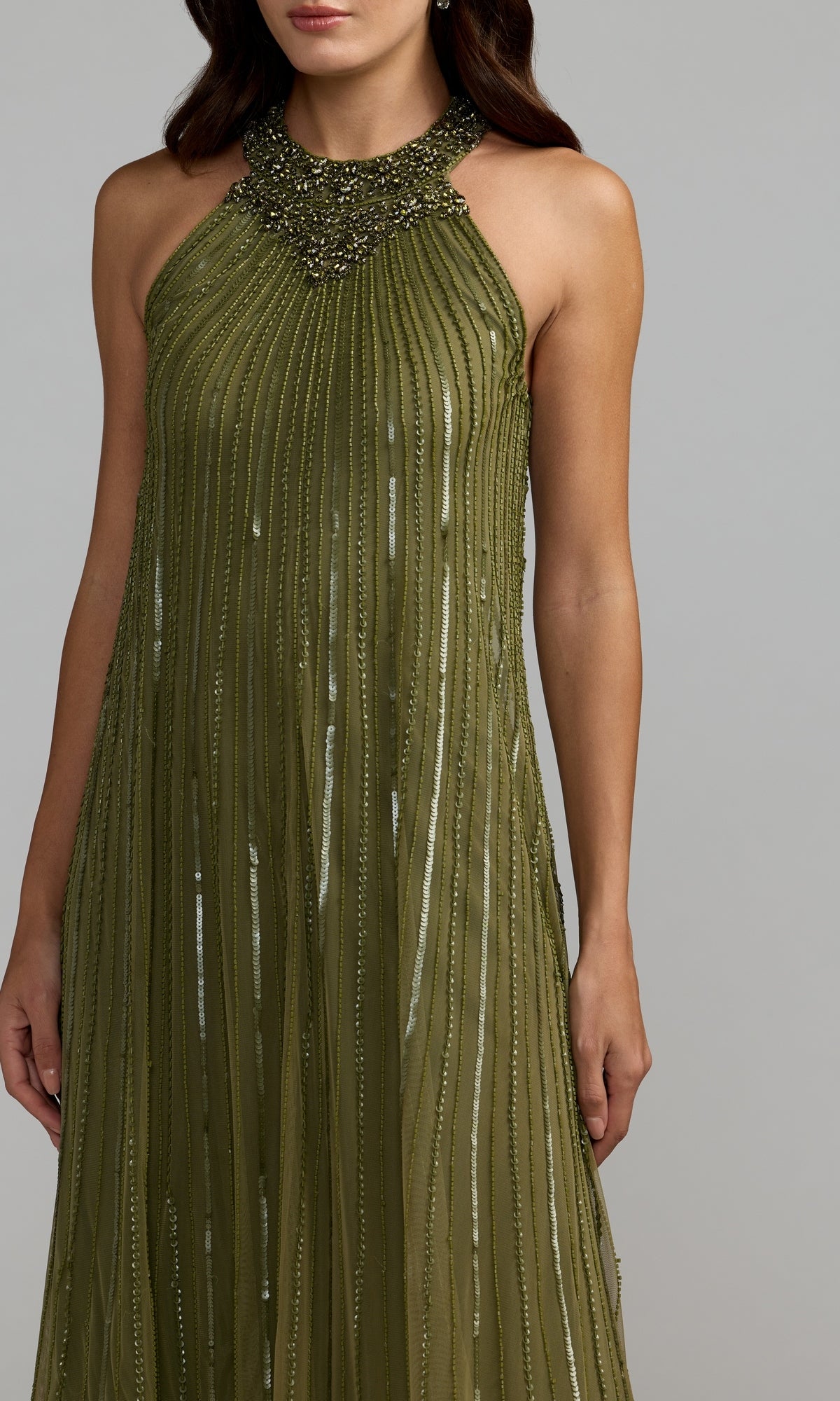 Woman wearing the Mac Duggal 23043 long formal dress in olive green, featuring a sleeveless design with a beaded neckline and vertical textured stripes, standing against a plain gray background. This look embodies the sophisticated elegance of Mac Duggal designs.