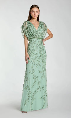 A woman poses with one hand on her hip against a plain background, wearing the Long Formal Dress: Mac Duggal 23067 in seafoam—a floor-length gown featuring short, sheer sleeves and exquisite floral embroidery.