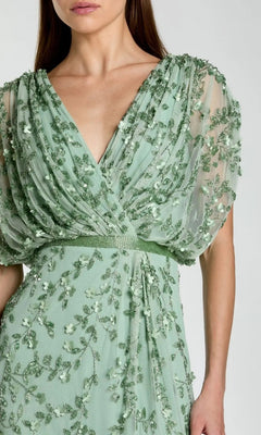 A woman models the Long Formal Dress: Mac Duggal 23067, featuring a light green sheer fabric adorned with embroidered beaded floral accents and a deep V-neckline, captured from shoulders to mid-thigh against a plain background for an elegant formal look.