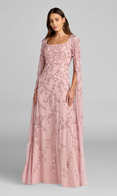 A woman wearing the Mac Duggal 23068 long formal dress in rose, featuring floral embroidery and cape sleeves, poses against a plain gray background.