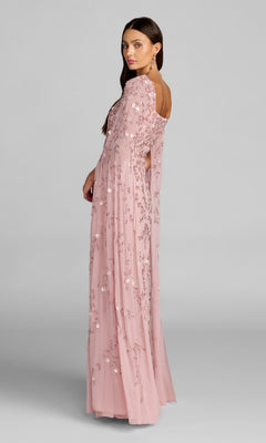 A woman stands sideways and looks over her shoulder against a plain gray background, wearing the Long Formal Dress: Mac Duggal 23068—a light pink gown with floral embroidery and sheer sleeves.