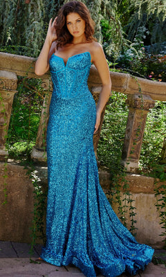 A woman stands outdoors in the Jovani Strapless Long Sequin Prom Dress 23077, featuring a fitted mermaid skirt, posing gracefully by a stone railing with lush greenery in the background.