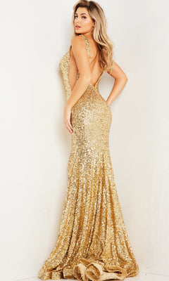 A woman poses in the Jovani Long Sequin Mermaid Prom Dress 23079, a sleeveless, backless, floor-length gold gown, against a plain light-colored wall.