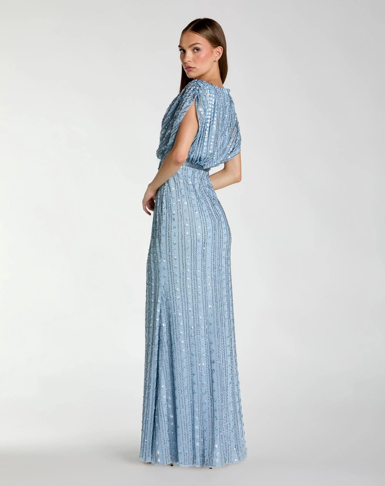 A woman stands sideways against a plain white background wearing the Mac Duggal 23081 Long Formal Dress—a sleeveless, floor-length gown in light blue with sequin embellishments and vertical stripes.