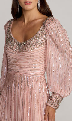 A woman wearing the Long Formal Dress: Mac Duggal 23085—a pink evening gown adorned with beaded embellishments and sequins, featuring a scoop neckline and puffed sleeves—creates an elegant look perfect for special occasions.
