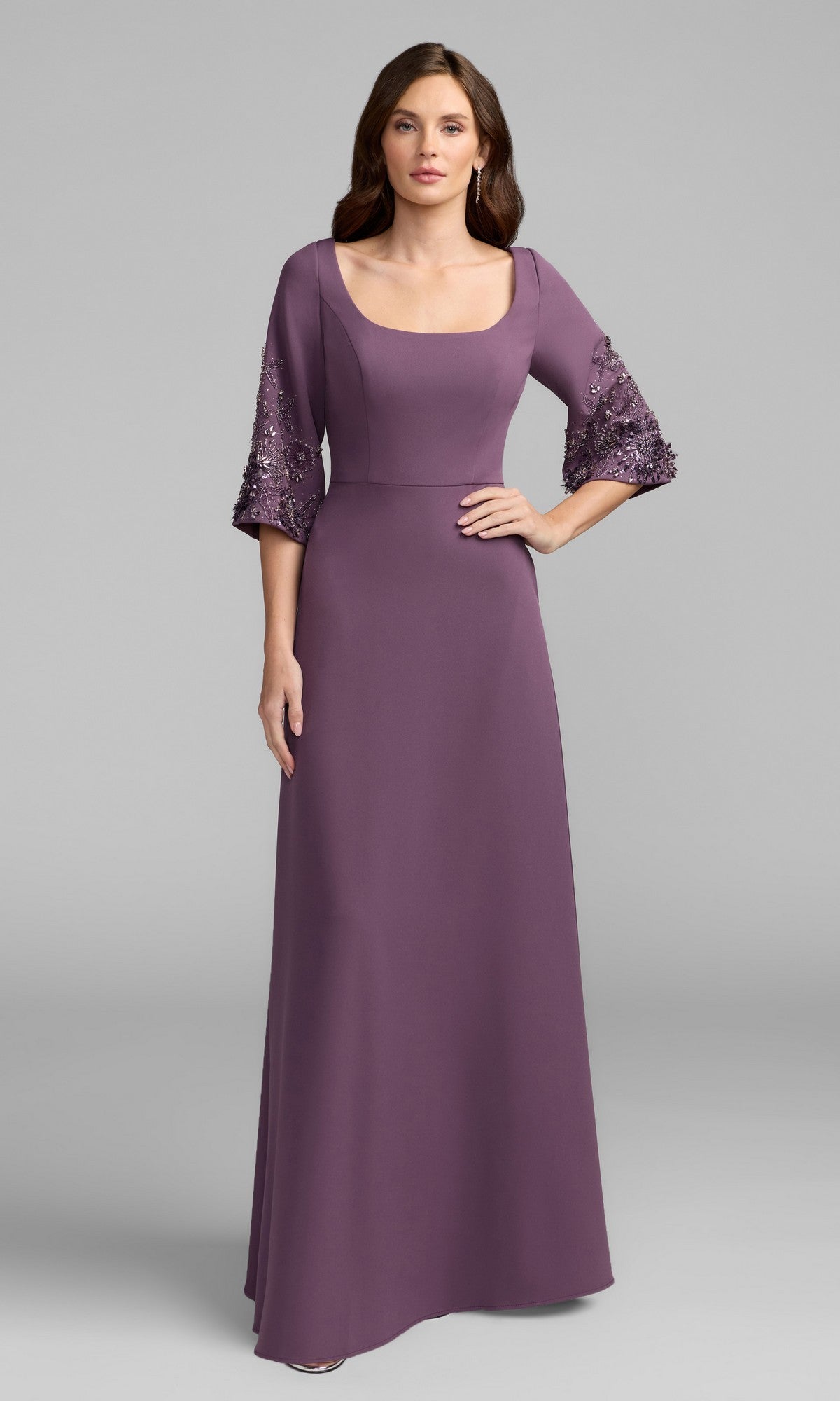 A woman stands against a plain gray background wearing the Mac Duggal 2311 Beaded-Sleeve Blue Formal Gown.