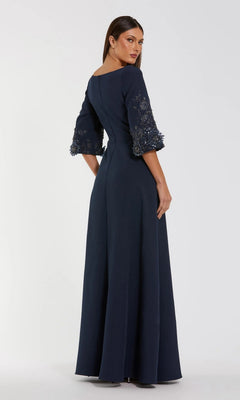 A woman in the Mac Duggal 2311 Long Formal Dress, a floor-length navy crepe gown with three-quarter sleeves, lace, and beaded details, stands against a plain light background, facing slightly away.