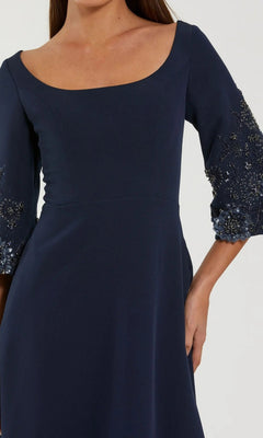 A woman in the Mac Duggal 2311 long formal dress, featuring navy crepe fabric, an elegant A-line silhouette, three-quarter sleeves, and beaded floral details at the cuffs.