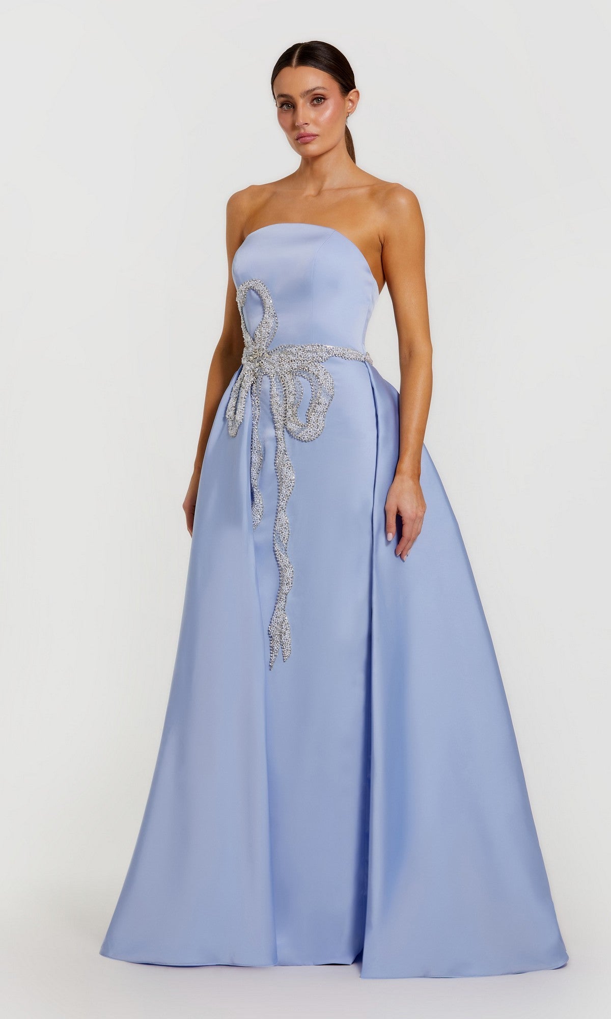 A woman models the Mac Duggal 2317 long formal dress in powder blue, featuring a strapless satin design and jeweled bow at the waist, standing against a plain white background.