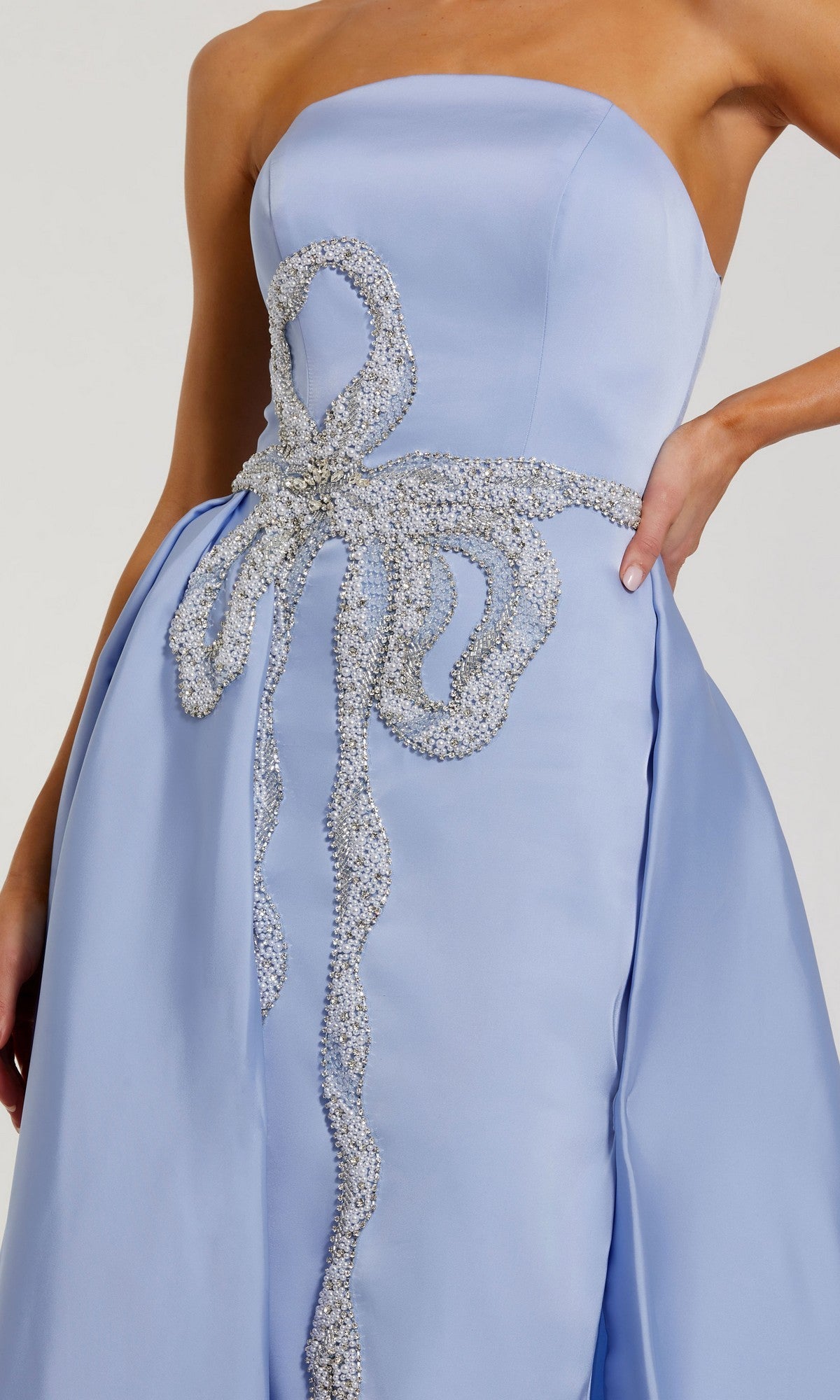 A person wearing the Mac Duggal 2317 long formal dress, a strapless light blue satin gown featuring a large decorative silver bow at the waist and hip.
