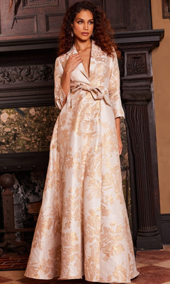 A woman stands indoors in front of a decorative fireplace wearing the Jovani 23178 long formal dress in gold.