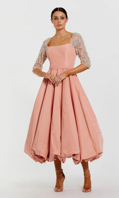 A woman models the Mac Duggal 2320 Semi-Formal Midi Party Dress in rose, featuring a square neckline, embellished mesh sleeves, bubble hem, and paired with strappy heels for an elegant look. Her hair is tied back.