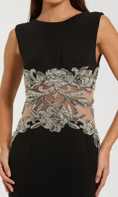 Woman in the Mac Duggal 2324 long formal dress, a sleeveless black designer gown with a beaded illusion waist, sheer panels, and intricate silver sequin and bead floral embellishments.