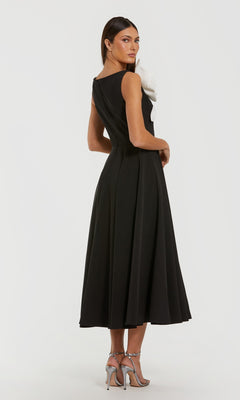 A woman poses against a plain white background wearing the Mac Duggal 2329— a sleeveless, tea-length black party dress with an elegant white ruffle detail on the front— paired with silver high-heeled sandals.