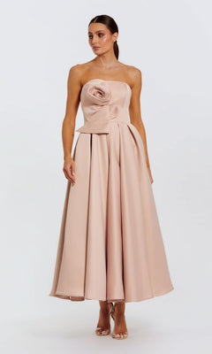A woman wears the Mac Duggal 2330 "Emerald" tea-length formal dress in rose pink, featuring a strapless bodice with a large rosette and pleated skirt, standing against a plain white background.