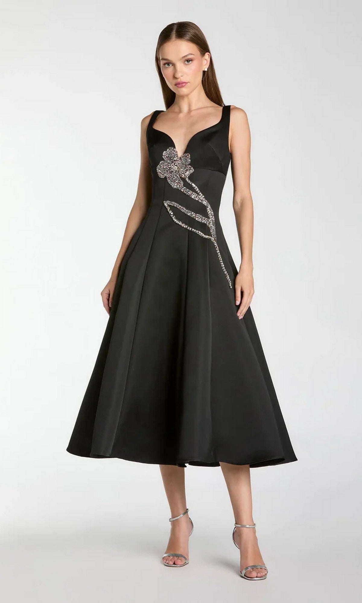 A woman stands against a plain background wearing the Mac Duggal 2331 Midi Party Dress, a sleeveless black satin midi dress featuring beaded-embellished floral accents on the bodice, paired with silver high-heeled sandals.
