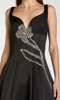A woman wearing the Midi Party Dress: Mac Duggal 2331—a sleeveless black satin midi dress featuring a plunging neckline and a prominent beaded-embellished flower on the front.