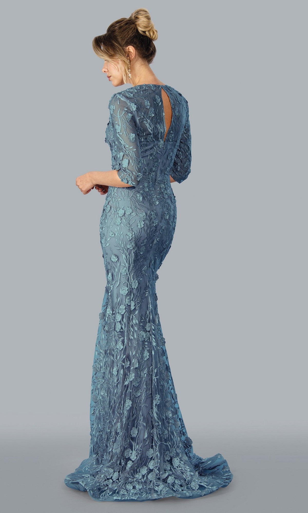 A woman is seen from the back wearing the Stella Couture 23311 long formal dress in slate, featuring elegant floral lace applique and three-quarter sleeves.