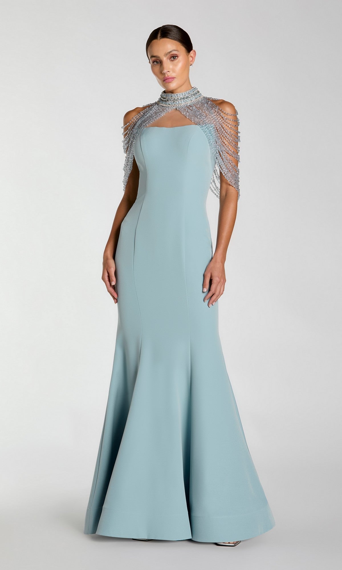 A woman wearing the Long Formal Dress: Mac Duggal 2334 in French Blue, featuring a fitted bodice, floor-length mermaid silhouette, and silver embellished shoulder detail, stands against a plain background.
