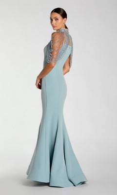 A woman in a fitted, floor-length Mac Duggal 2334 long formal dress in light blue, featuring beaded short sleeves and a mermaid silhouette, stands against a plain light background, posed slightly away from the camera.