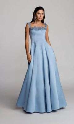 A woman wearing the Mac Duggal 2337 long formal dress in slate blue, featuring a floor-length A-line silhouette and floral strap details, stands against a plain gray background.