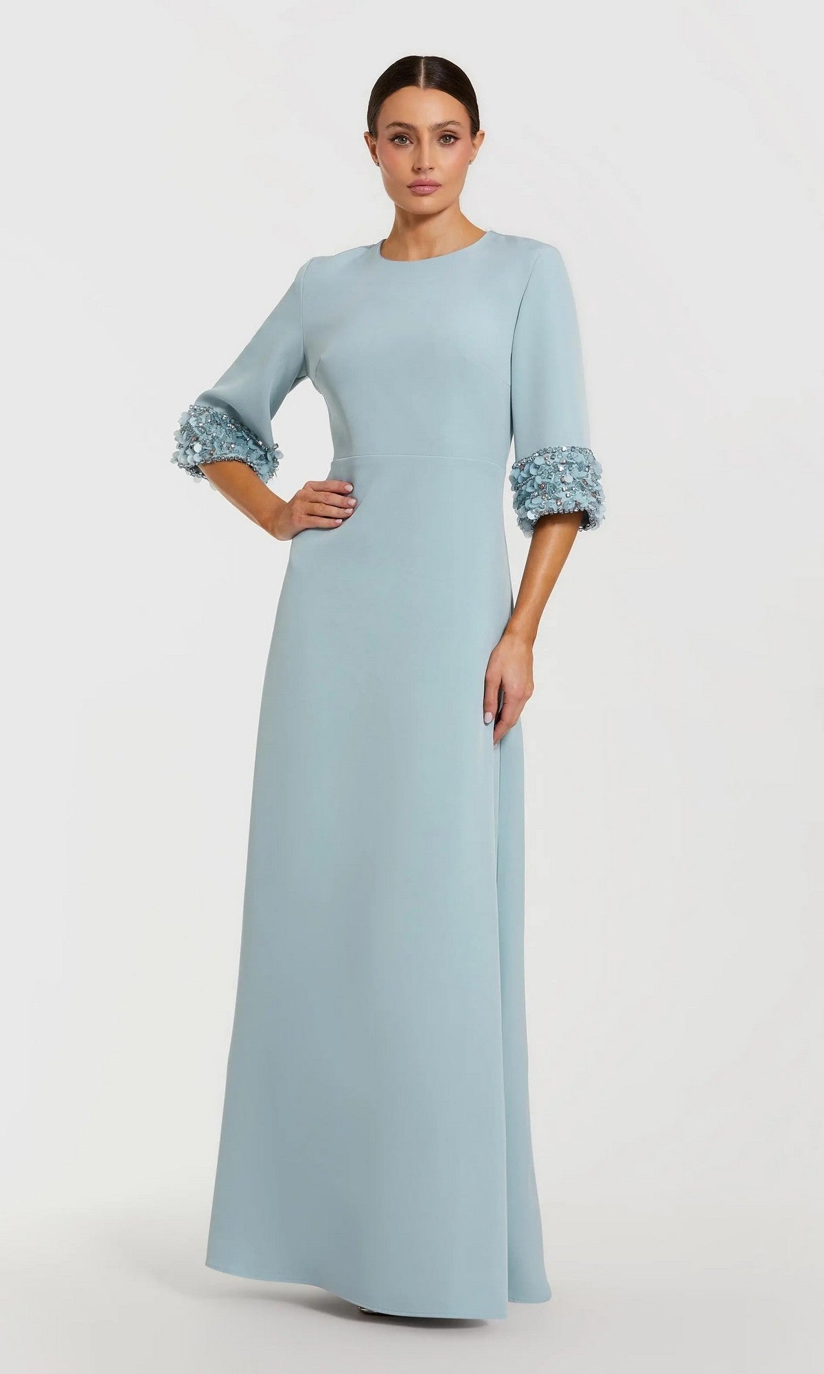 A woman stands wearing the Mac Duggal 2342 long formal dress in French Blue, a floor-length evening gown with three-quarter sleeves and decorative beaded cuffs that add an elegant touch to this modest design.