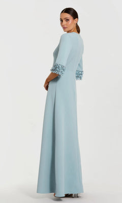 A woman poses against a plain background, looking over her shoulder in the Mac Duggal 2342 Long Formal Dress—a floor-length, light blue evening gown with flared sleeves adorned with floral embellishments and delicate beaded cuffs.