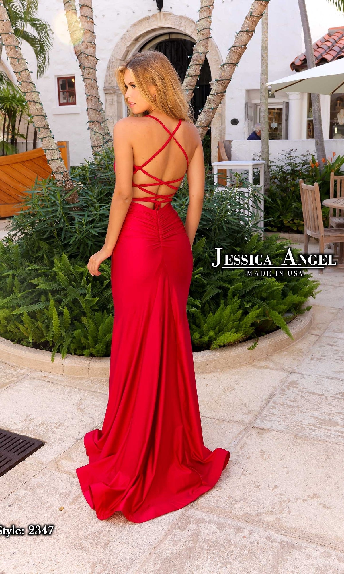 A woman stands outdoors before greenery, wearing the Jessica Angel 2347 Lace-Up Long V-Neck Prom Dress—a floor-length gown with crisscross straps, perfect for formal events and special occasions.