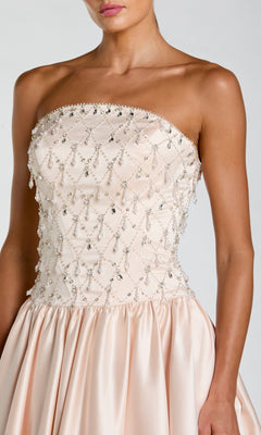 A woman wearing the Mac Duggal 2354 long formal dress, a strapless satin gown in light pink with a fitted, beaded bodice and a flared skirt.