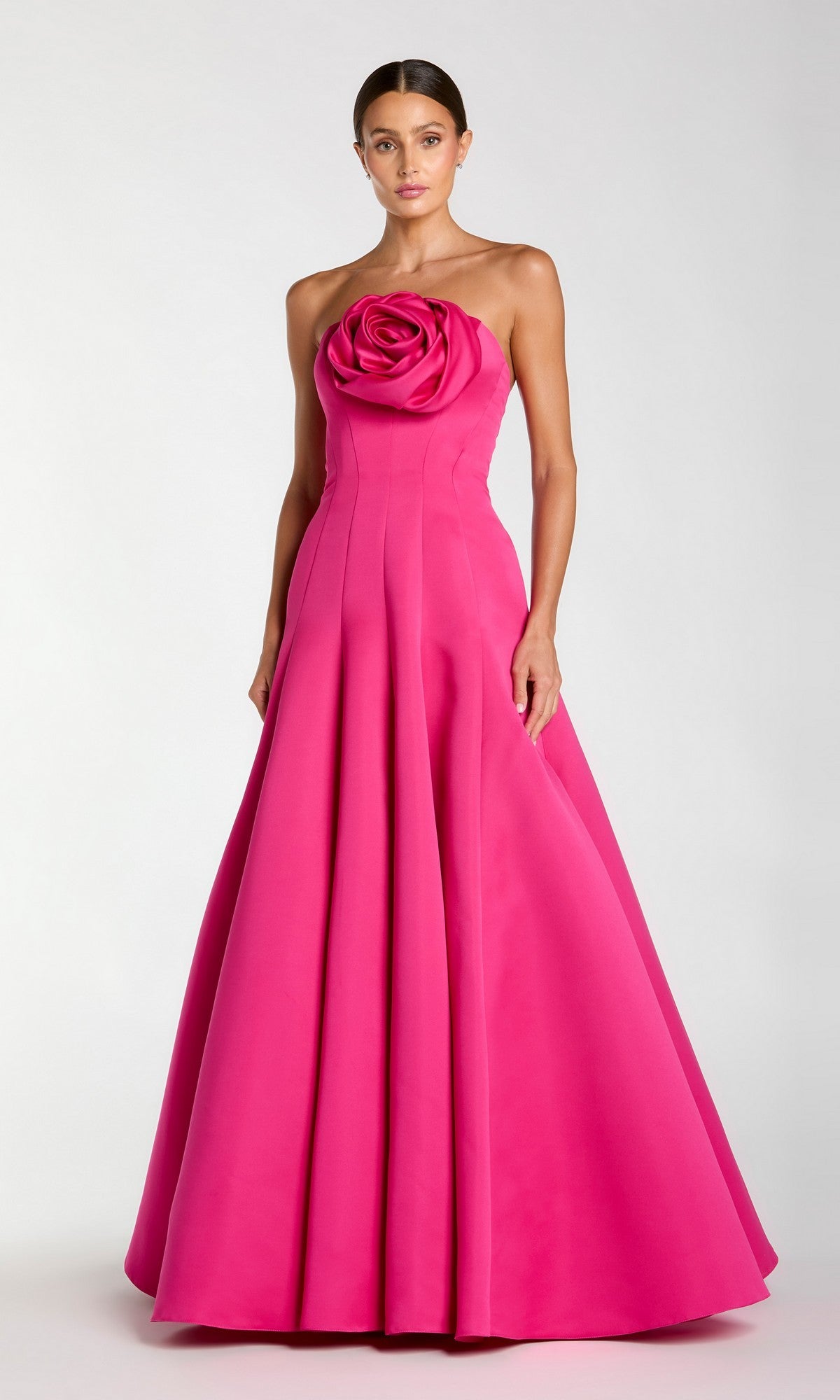 A woman wearing the Mac Duggal 2357 long formal dress in fuchsia, a strapless floor-length crepe-satin gown with a large rose detail at the bodice, stands against a plain background.