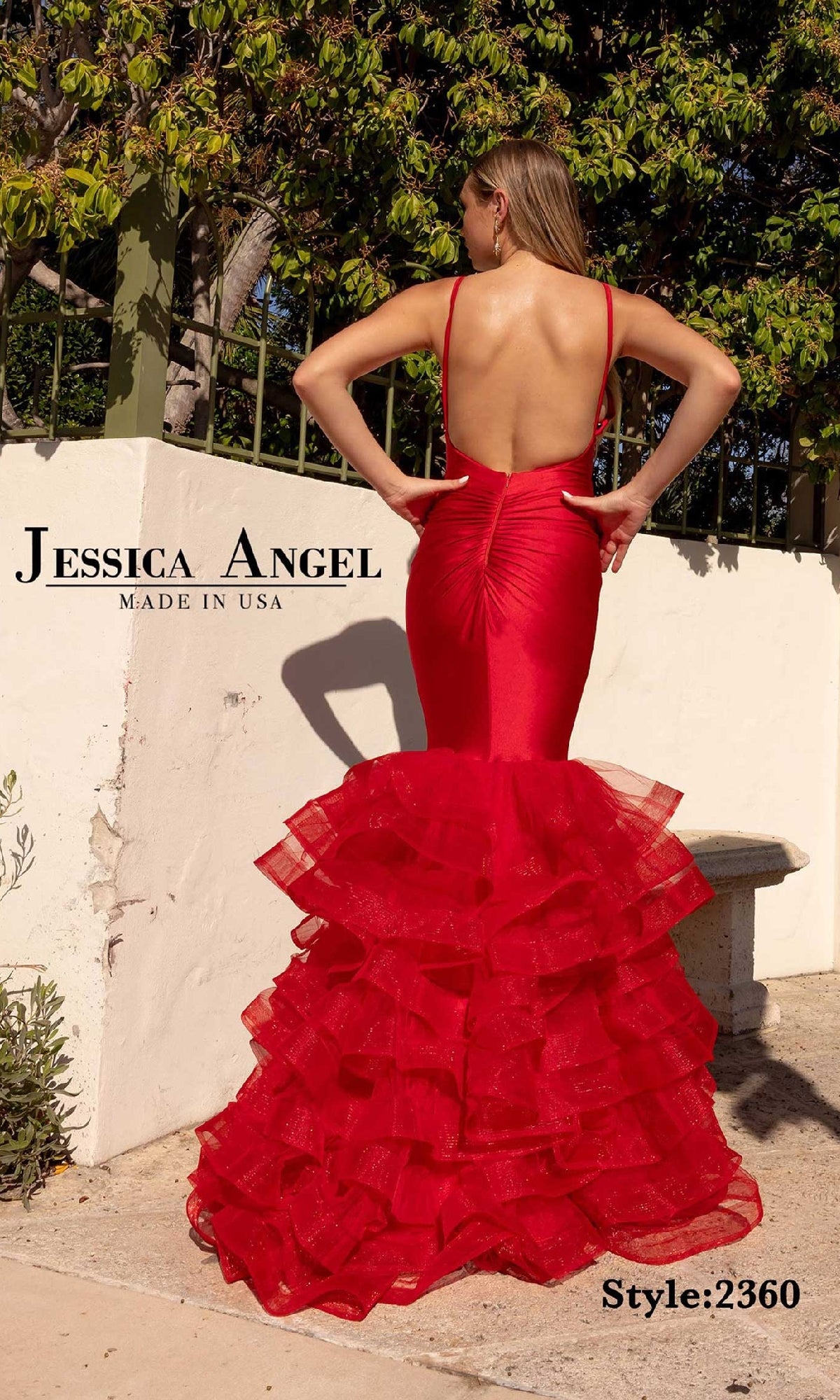 A woman stands outdoors facing away, wearing the Long Prom Dress with Ruffles: Jessica Angel 2360—a fitted, bright red mermaid gown featuring ruffled tulle layers.