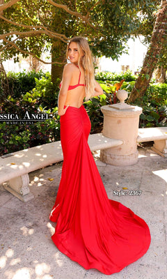 A woman in a floor-length, backless criss-cross gown—Jessica Angel 2369—stands outdoors by greenery and a stone planter, looking over her shoulder.