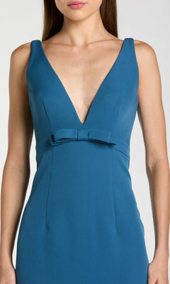 A woman wearing the Mac Duggal 2371 Long Formal Dress—a sleeveless, deep V-neck blue fit-and-flare gown with a small waist bow.