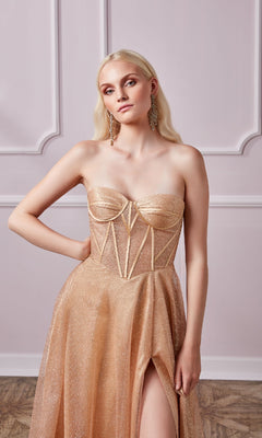 A woman in the Aerie Couture 237 Long Glitter Corset Prom Dress, featuring a strapless design, structured bodice, corset back, and high slit, stands against a light pink ornately paneled wall.