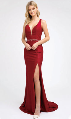 A woman models the Juliet 237 long prom dress, a deep red, form-fitting gown with a plunging neckline, beaded waistband, high slit, strappy back, and floor-length hem as she poses before a plain white background.