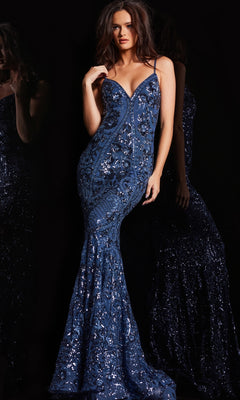 A woman wearing the Jovani V-Back Long Sequin-Print Prom Dress 23839 in deep blue, featuring thin straps and a mermaid silhouette, stands against a dark background.