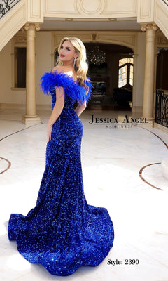 A woman in a royal blue, off-the-shoulder Feather Long Sequin Prom Dress (Jessica Angel 2390) with sequin and feathered trim stands in an elegant interior. Made in USA—perfect for your special night.