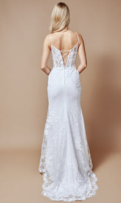 A woman with long blonde hair models the Nina Canacci 2392, a long formal dress with a fitted silhouette, thin straps, and a lace-up corset back, standing against a beige background.